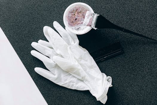 Flat lay of hairdressing tools including dye brush, latex gloves, hair dye bowl, and comb.