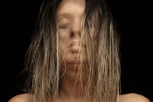 An artistic close-up portrait of a woman with wet hair, eyes closed, on a dark background.